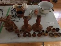 Overview photo of lot items on a white table, including wood candleholders, ceramic vase and bowl, electric water feature, chamber pot, and wooden windmill.