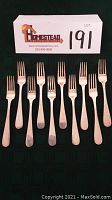 Ten silver forks arranged in a row on black fabric with lot tag