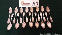 Set of 15 antique tablespoons arranged on dark fabric, clearly showing the spoons' overall shape and design.