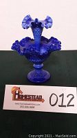 Front view of deep blue hobnail glass epergne with ruffled rim and central trumpet horn