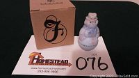 Front view of the snowman figurine next to its original box and lot number card on a black surface.