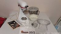 KitchenAid stand mixer with attachments and booklet displayed on table.