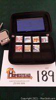 Opened carrying case with folded blue DS Lite in upper compartment and seven game cartridges in lower slots.