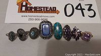 Photo of all eight sterling silver rings lined up horizontally showing stone colors and shapes.