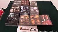 Overall view of the 9 seasons of The X-Files DVD box sets laid out with Fight The Future movie box also included. Several seasons unopened as indicated by shrink wrap.