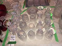 Four different sets of crystal glasses arranged on table with varied cut patterns and shapes, including stemmed and non-stemmed glasses.