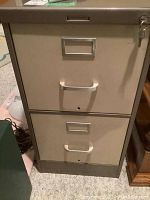 Front view of beige two-drawer metal filing cabinet with recessed handles and keys in lock.