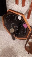 Photo of the magnetic dart board leaning against stairs with cylindrical container in front.
