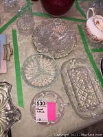 Top view showing a sizable round glass bowl with scalloped edges and floral etchings, round plate with geometric starburst design, a rectangular dish with quilted diamond motifs, and a small handled round menu or serving dish.