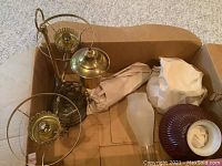 Photo showing lamp components including brass lamp base, lamp holders, and exposed wiring with scattered wrapped paper.