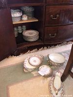Wide view of sideboard interior showing stacks of plates and bowls with additional pieces on floor.