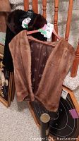 Front view of brown mink fur vest hanging on a wooden rack, showing soft fur texture and lining.