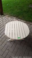 Round white wooden table with slatted top surface showing minor paint chipping, placed on a paved outdoor patio.