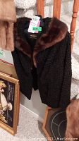 Black Persian lamb fur stole with brown fur collar hanging, tag visible with size and label