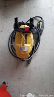 Yellow Karcher pressure washer sitting on floor with attached black power cord and pistol grip handle.