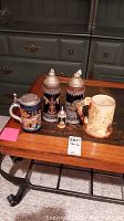 Photo of four German beer steins on wooden coffee table, showing diverse designs and lids.