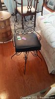 Stool with black seat cushion, decorative wire back and arms, metal frame, and metal feet on hardwood floor.