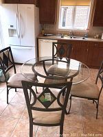 Full view of round glass dining table with four metal chairs and beige cushions in kitchen setting.