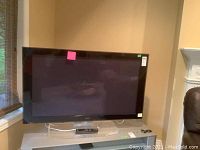 Front view of 50 inch flat-screen plasma TV on stand showing black frame and dark screen. Several stickers on screen edges.