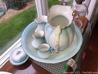 Wash basin set including large washbasin, pitcher, small creamer and bowl, chamber pot with lid on wooden surface near window, showing glazing and repair details.