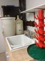 Photo showing large plastic fermentation bucket, plastic carboy, and glass carboy on the counter with sink in foreground.