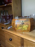 Wooden octagonal sewing box showing front with leaf decoration and metal latch closed on wooden surface.