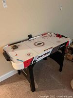 Overtime Hockey air hockey table with folding legs, red pushers and puck, black legs, and white top with red and black graphics.