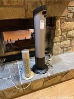 Two appliances on stone hearth: taller black Seville Classics heater and shorter silver Sharper Image air purifier with white cord.