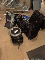 Photo showing multiple bags including garment bag, cooler backpack, duffel bag, and tote bags on floor