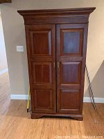 Exterior front view of closed cabinet showing crown molding, paneled doors and brass-tone handles