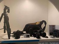 Wide shot of all items on table including tripod, cameras, lenses, bags, video and wildlife cameras.