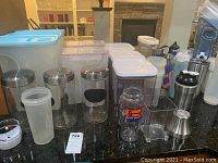 Photo showing plastic storage containers, stainless steel canisters, cylindrical glass storage container, insulated cups, and kitchen utensils on countertop.