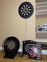 Overall lot of four dart boards including two mounted dart boards, one standard dart board, and one boxed electronic dart board.