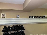 Multiple framed sports memorabilia photographs displayed on a shelf above dumbbells in a room