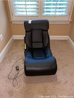 Front view of black gaming chair with padded seat and leg rest, placed on carpeted floor near window.