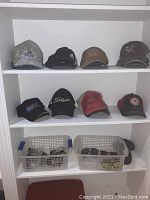 Shelf showing several baseball hats including Adidas camo, black Adidas, Oakley brown and Vortex black hats