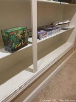 Wide shelf view showing green Ixalan bundle box left and white board game box right