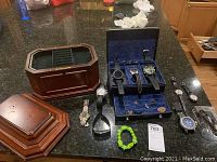 Overview showing wooden jewelry box, travel case, five watches, fitness band and accessories on countertop