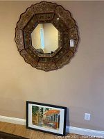 Wall mirror hung on the wall with the framed poster leaning against the baseboard on the floor beneath it.
