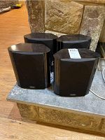 Four black Polk Audio RM 7500 bookshelf speakers with curved edges and black cloth front covering.