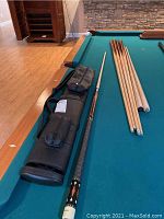 Overview on pool table: assembled cue, extra shafts, case