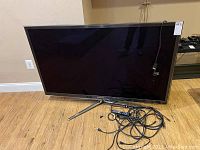 Front view of Samsung plasma TV with remote and cables on floor
