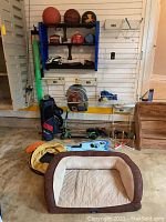 Overview of all items in lot including sports balls, helmets, gloves, golf clubs, boogie board, scooter, backpack, fishing gear, and pet bed.