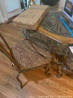 Image showing one of the four chairs next to the round glass top table base, highlighting the patterned upholstery and wood/metal legs with claw feet.