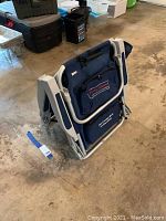Folded navy blue Tommy Bahama beach chair with white metal frame on floor.
