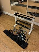 Weight rack positioned on wooden floor next to mirror with multiple resistance bands and handles coiled beside it.