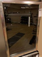 Front view of Haier wine cooler showing glass door with stainless steel frame and Haier logo.
