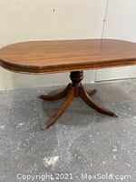 Walnut coffee table showing oval top and Duncan Phyfe style pedestal legs on concrete floor.