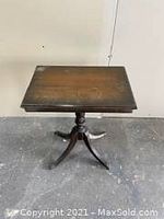Front view of antique wooden side table showing rectangular top, single central pedestal, and curved legs with brass claw feet.