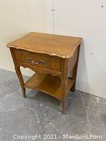 Side view of the solid wood side table showing drawer front, scalloped edges of the top, straight legs, and bottom shelf.